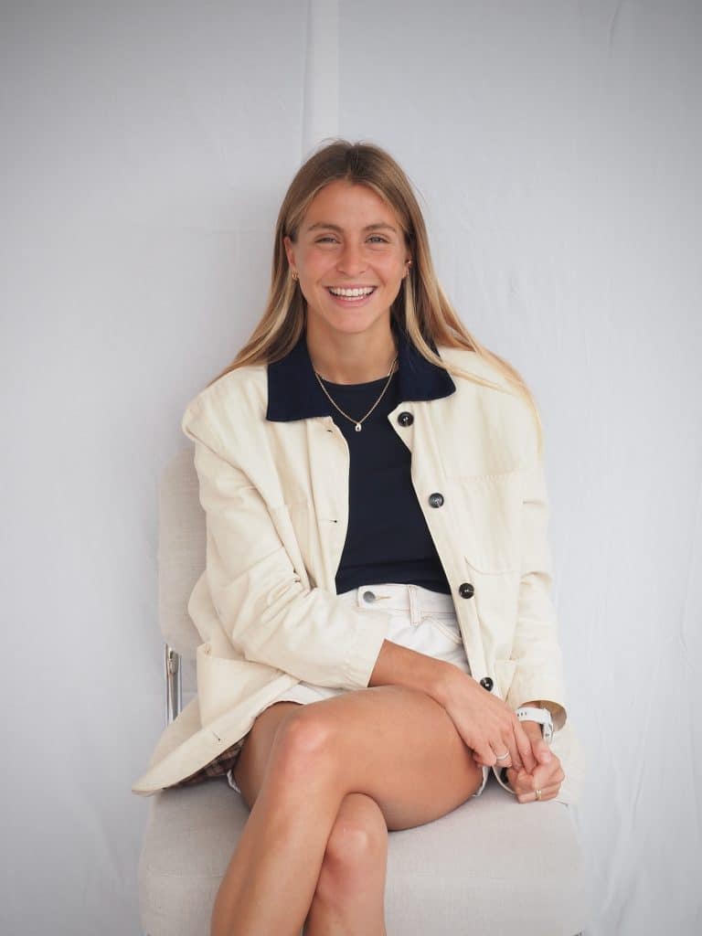 Photo d’Églantine Lanier assise sur une chaise devant un fond blanc, illustrant son rôle d’accompagnatrice de projets digitaux et d’experte en stratégie web