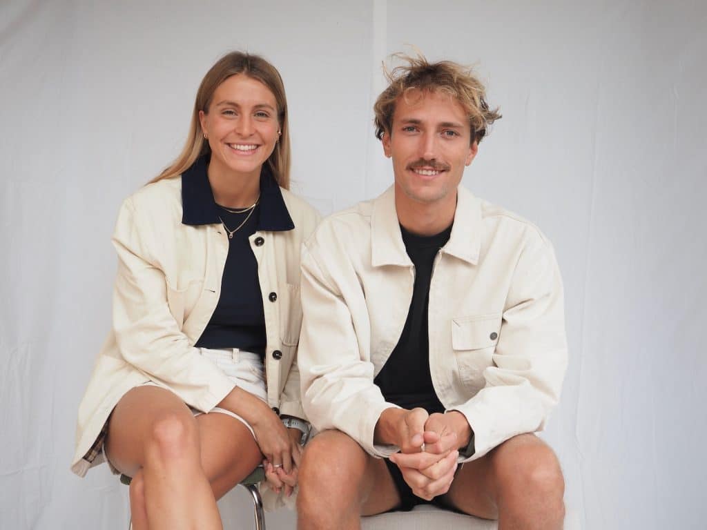 Photo de l’équipe agence digitale hossegor, Robin Canton Lamousse et Églantine Lanier assis sur une chaise devant un fond blanc, illustrant leur collaboration pour des projets web et applications sur-mesure